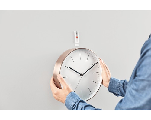 Person som fäster en rund väggklocka på väggen med en självhäftande spik.