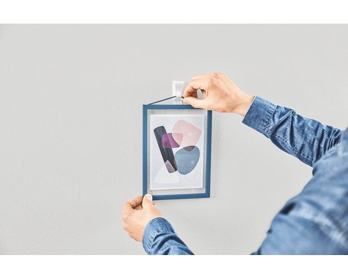 En person hänger en inramad bild på en vägg med en självhäftande krok.