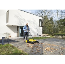 Man sopar löv med en sopmaskin framför ett bostadshus.