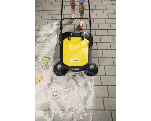 Gul sopmaskin i bruk på stenläggning med sand och barnleksaker.