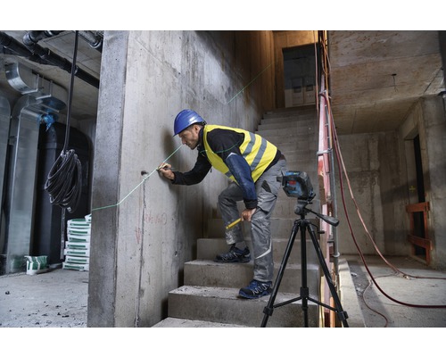 En byggnadsarbetare använder en linjelaser på en byggarbetsplats för att markera en rak linje på en betongvägg.