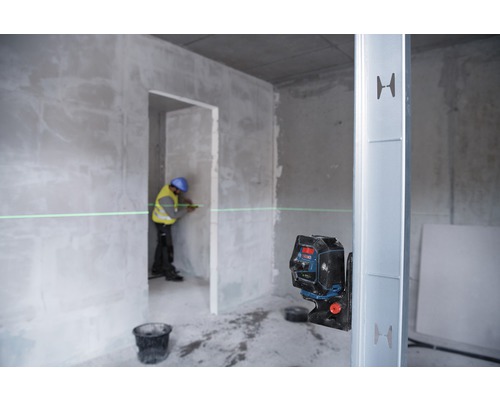 En arbetare använder en linjelaser i ett oinrett hus för att markera en rak linje på en vägg.