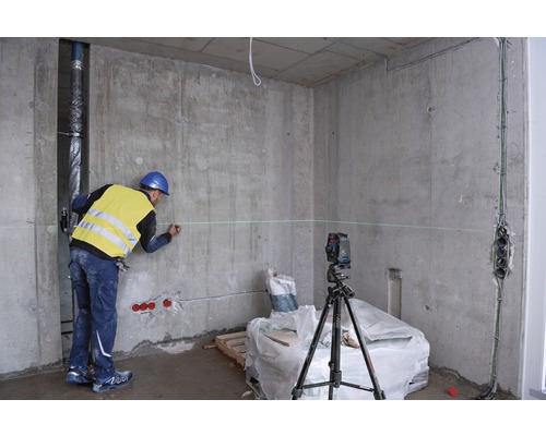 Byggnadsarbetare markerar vägg med laserpass i ett oinrett rum