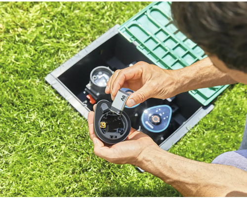 Person sätter ett batteri i en bevattningsdator i trädgården