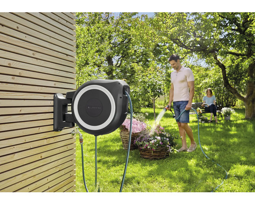 Trädgårdsslangbox monterad på en trävägg med en man som vattnar blommor.