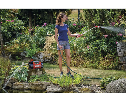 Kvinna vattnar trädgård med trädgårdspump och trädgårdsslang