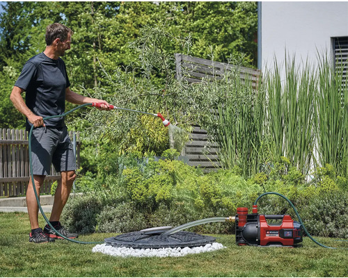 Man vattnar trädgården med trädgårdspump och slang