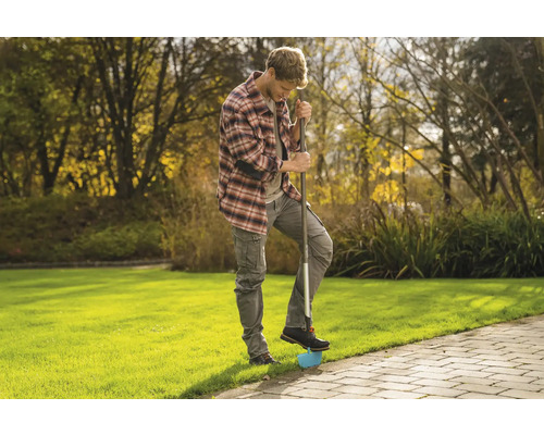 En man använder en gräskantstickare i trädgården för att bearbeta gräskanter