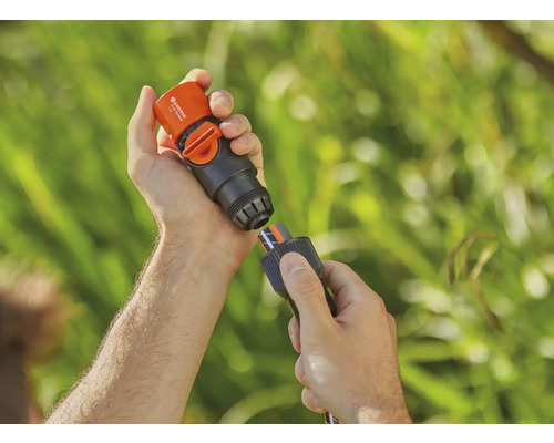 En person ansluter en Gardena vattenstoppskoppling till en trädgårdsslang.