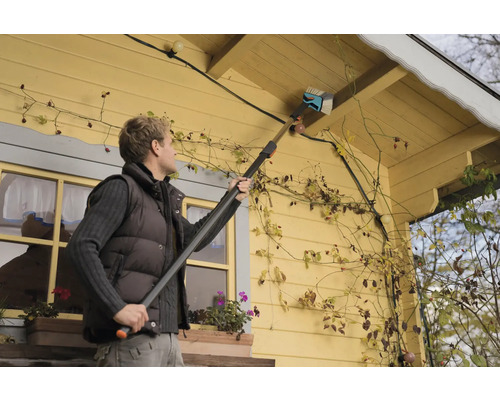 En person rengör ett hustak med en takrännsborste.