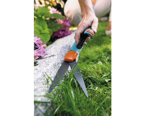 Person klipper gräs med en gräskantsax längs en sten