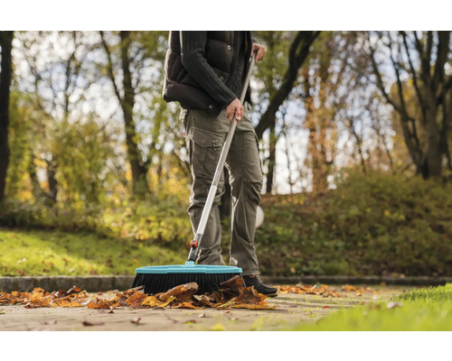 En person sopar löv med en gatukvast utomhus.