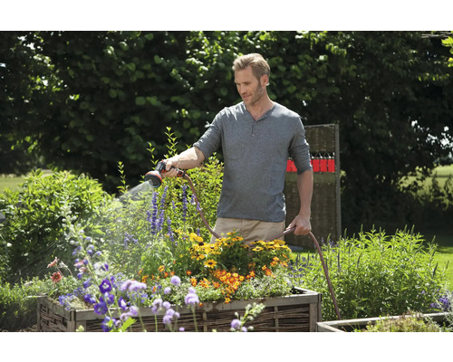 En man vattnar blommor med en trädgårdsslang i trädgården.