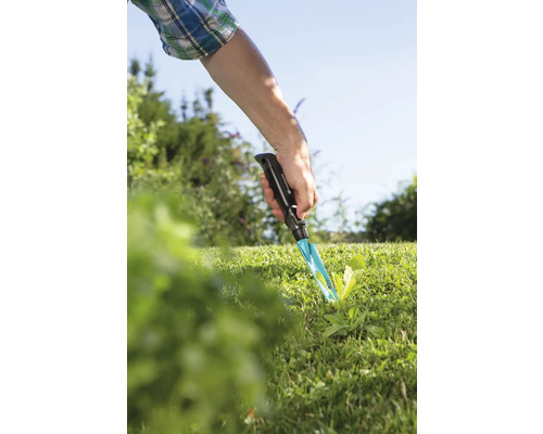 Trädgårdsscen med en hand som använder ett ogräsjärn i gräsmattan