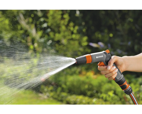 En hand håller i en trädgårdsspruta som sprutar vatten.