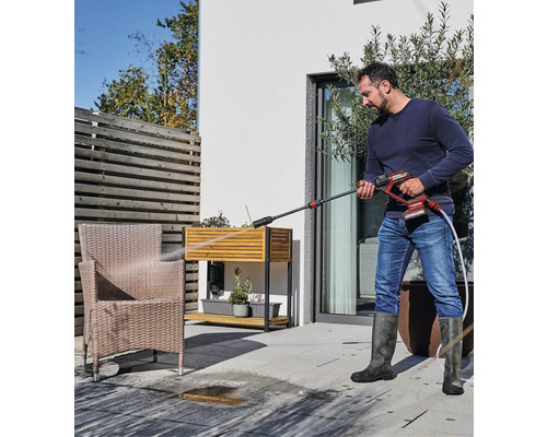 Man rengör en uteplatsstol med en sladdlös högtryckstvätt utomhus.