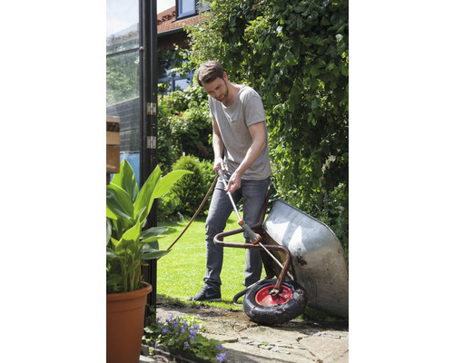 Man rengör en skottkärra med en trädgårdsslang i trädgården.