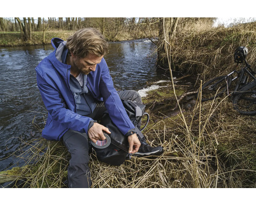 Man med tejp vid en flodstrand, bredvid en cykel.