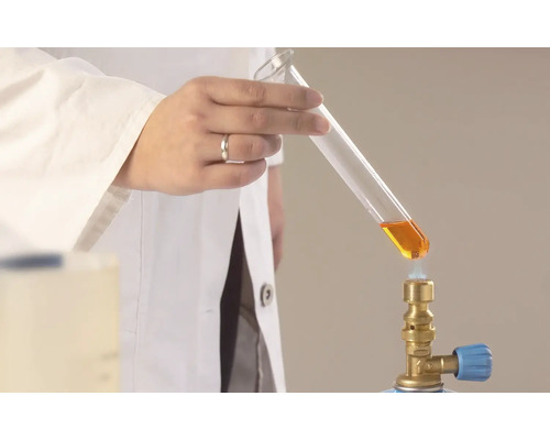 En laboratoriearbetare värmer en vätska i ett provrör med en gasbrännare.