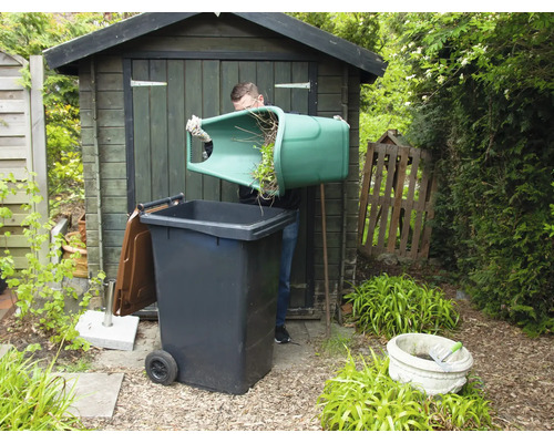 Man tömmer trädgårdsavfall i en avfallsbehållare i trädgården