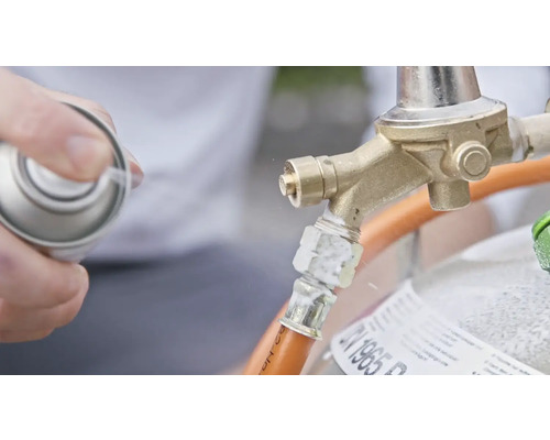 En person sprayar läckagesökningsspray på en gasventil för att kontrollera om det finns läckor.