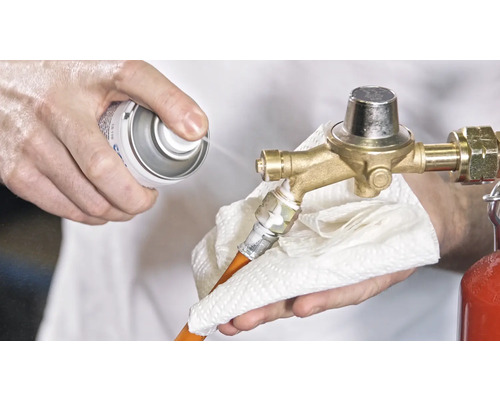 En person rengör en gasolregulator med en spray och en trasa.
