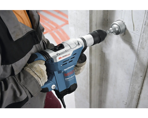 En man borrar ett hål i en betongvägg med en Bosch borrhammare.