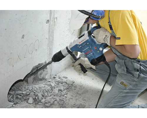 En arbetare använder en borrhammare för att borra ett hål i en betongvägg.