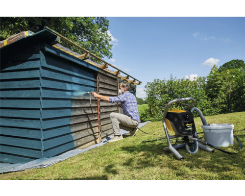 Man målar trähus med färgspruta