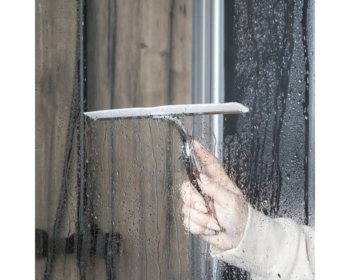 En person använder en duschskrapa för att rengöra en duschvägg.