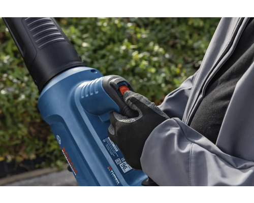 En person använder en lövblås i trädgården.