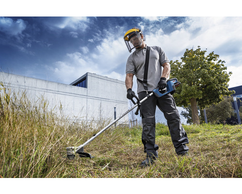 En person använder en grästrimmer med skyddsvisir i trädgården.