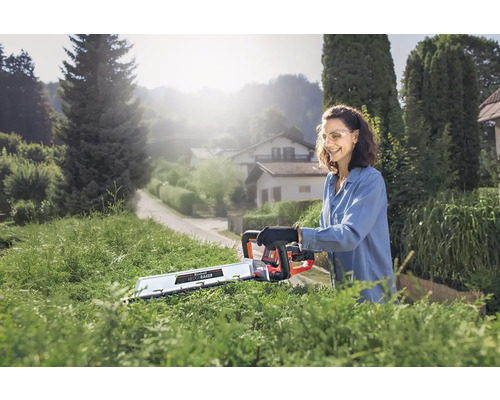 Kvinna klipper häck med en batteridriven häcksax i trädgården.