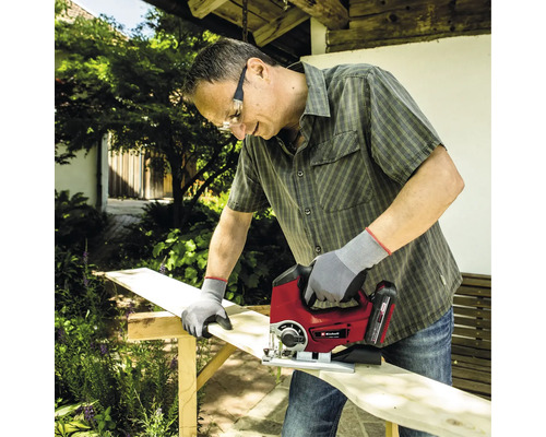 Man sågar träbräda med sticksåg i trädgården