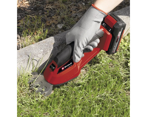 En person använder en Einhell batteridriven grässax för att klippa gräs längs en gräsmatta.