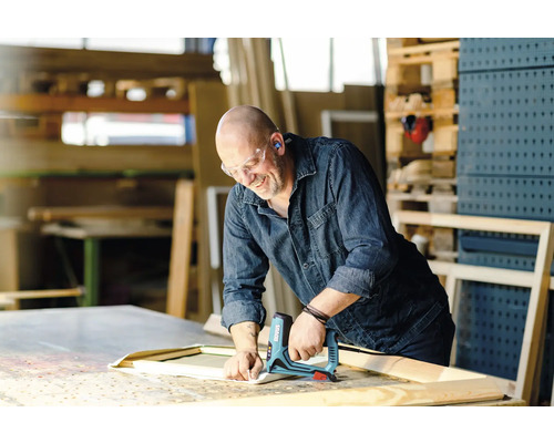 En hantverkare fäster tyg med en elektrisk häftpistol på en träram i en verkstad.