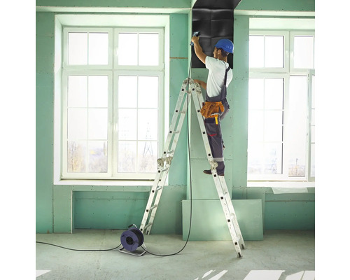 Hantverkare på en stege fäster ljudisoleringsskivor på en vägg i ett rum.