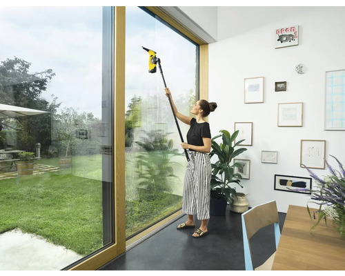 Kvinna rengör fönster med en fönstertvätt inomhus.