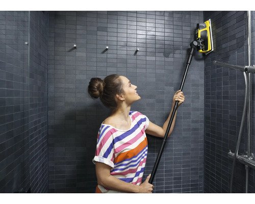 Kvinna rengör en kaklad dusch med en fönsterskrapa med teleskopskaft