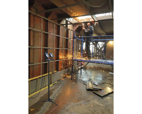 En arbetare står på en ställning och skär metall med en skärmaskin, med gnistor som flyger.