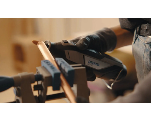 En person använder ett Dremel 8240 multiverktyg för att skära ett kopparrör som är fastspänt i ett skruvstäd.