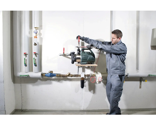 Installation av en trädgårdspump av en hantverkare på en vägg med rör.