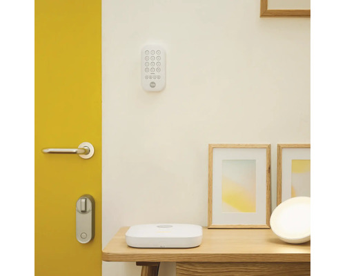 Scen med digitalt dörrlås, knappsats, basstation och fotoramar på ett bord