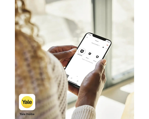 Person som använder Yale Home-appen på en smartphone för att styra larmsystemet.