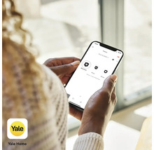 En person använder Yale Home-appen på en smartphone för att styra ett larmsystem.