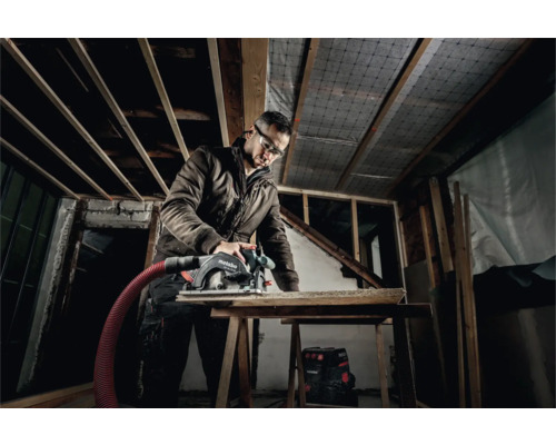 Hantverkare med skyddsglasögon sågar trä med en cirkelsåg från Metabo i ett oinrett hus.