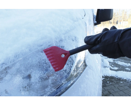 En person tar bort is från en bilruta med en isskrapa.