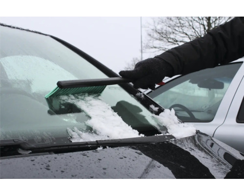 En person tar bort snö från en vindruta med en isskrapa.