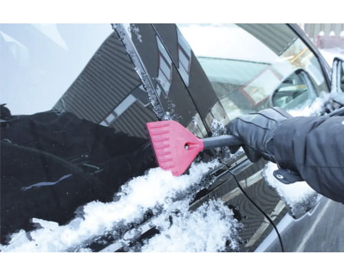 En person tar bort is från en bilruta med en isskrapa.