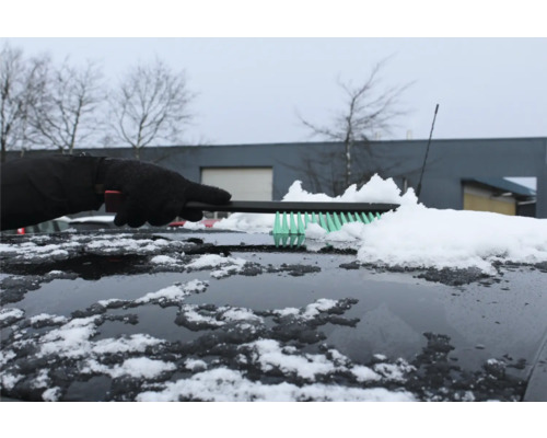 En person tar bort snö från en bils tak med en borste.